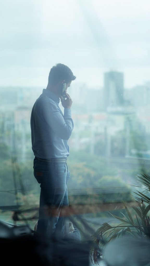 Side profile of a businessman on a phone call inside an office with a cityscape view.