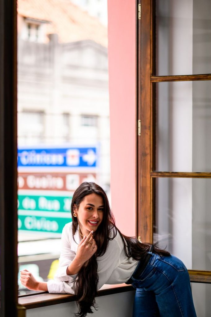 A young woman leans by a window in an urban setting, showcasing fashion and style.